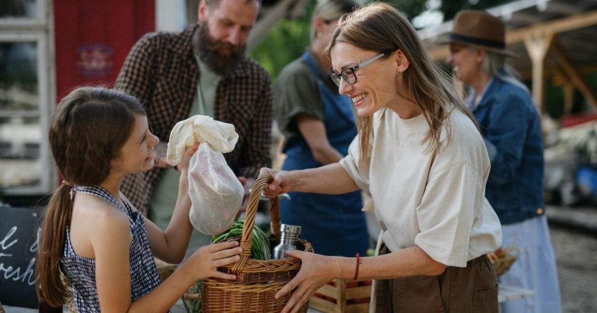 Little girl with her mother buying organic vegetables outdoors at community farmers market