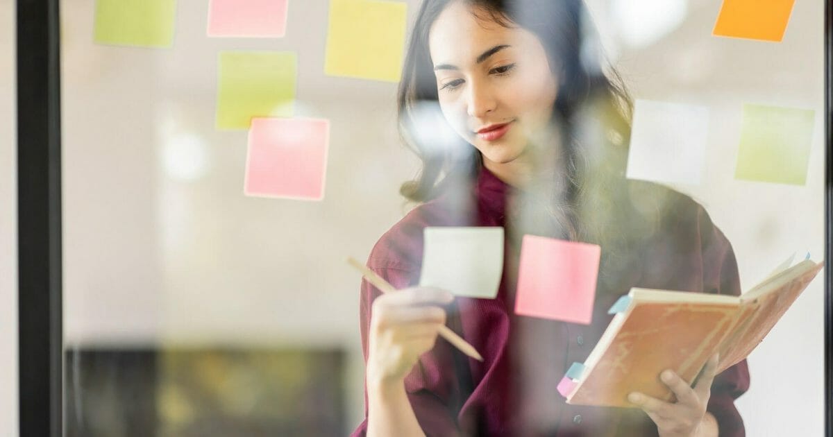 Business female employee with many conflicting priorities arranging sticky notes commenting and