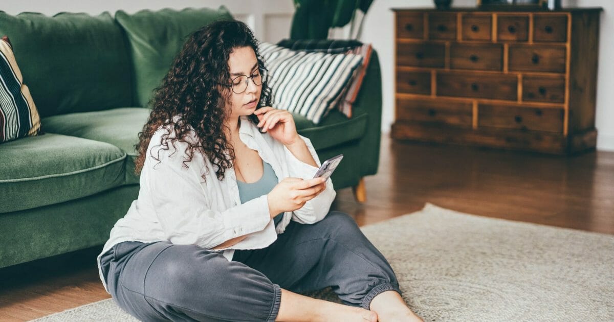 woman wearing comfortable clothes in glasses clicks on smartphone screen sitting