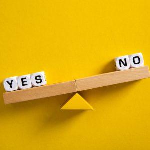 Yes vs No. Choice concept. Balance scales on yellow background. Close up.